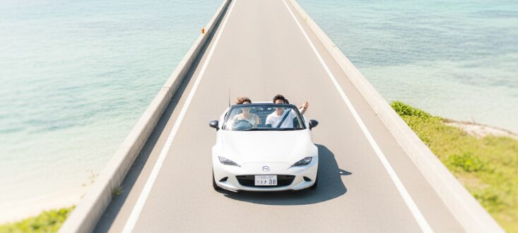 沖縄の青い海の上をオープンカーで爽快にドライブするカップル。海中道路で楽しむ地元ならではの沖縄デート。