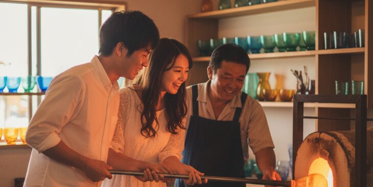 沖縄の工房で琉球ガラス作りを体験するカップルと職人。思い出に残る体験ができる地元デートに人気のスポット。