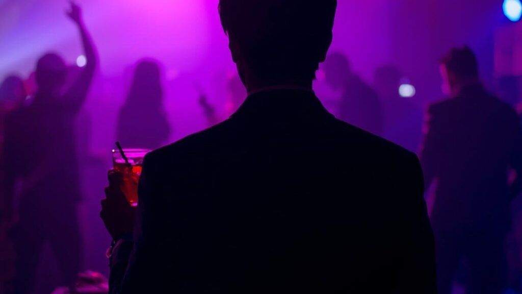 松山のクラブやDJバーで、フロアの様子を伺う男性のシルエット。沖縄一人旅でワンナイトや男の出会いを期待させる、大人の夜遊びスポットのムーディーな空気感。