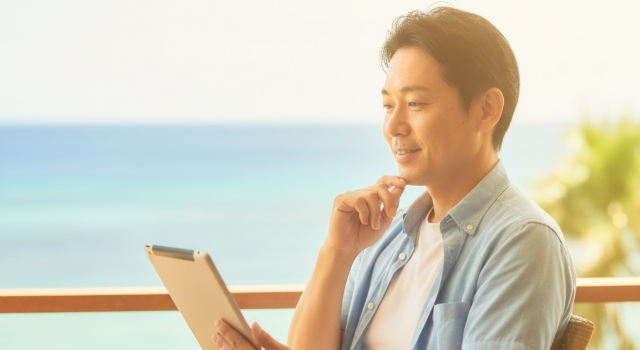沖縄のカフェでタブレットを使い、自分に合ったマッチングアプリをランキングで比較検討する40代男性。