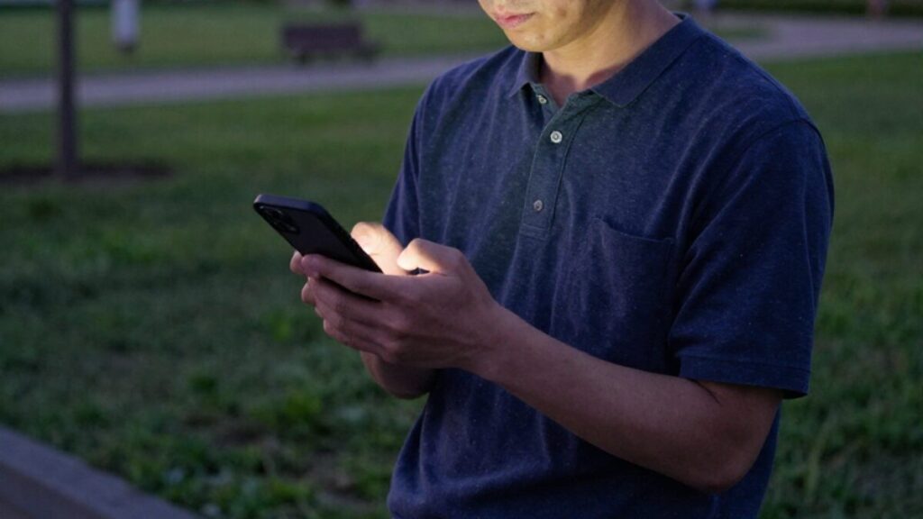 夕暮れの公園で、自分に合ったプラットフォームを思案しながらスマートフォンを操作する男性。マッチングアプリの日記活用術を最大限に活かせる場所選びを象徴する画像。