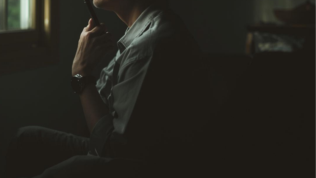 窓辺で静かに思索にふけりながら、マッチングアプリのプロフィール文に書く性格やエピソードを整理している男性の横顔。