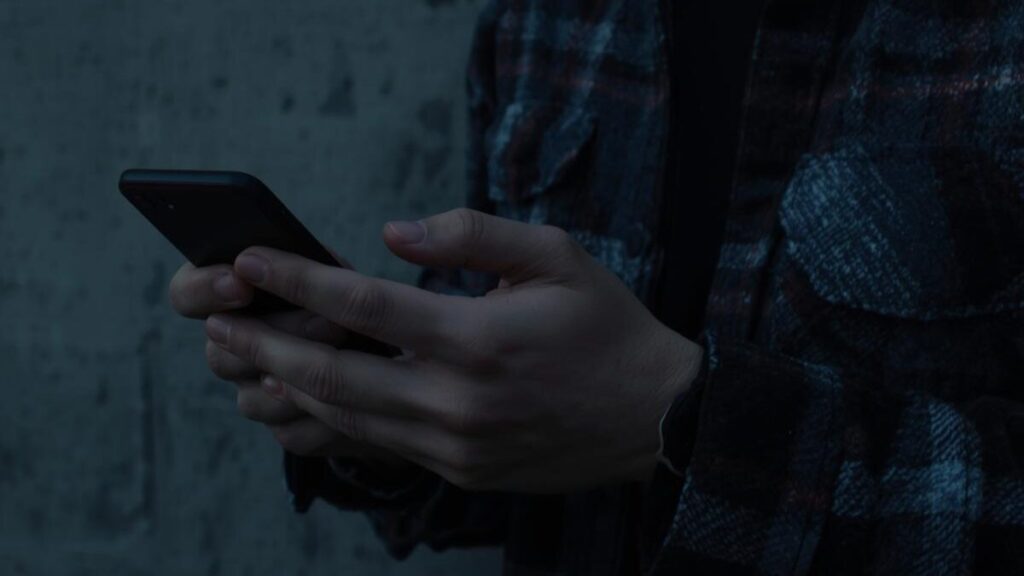 スマートフォンを手に持ち、通知を待っている日本人男性の手元。電話番号認証などの手続きを行い、マッチングアプリの安全性を確保しているシーン。