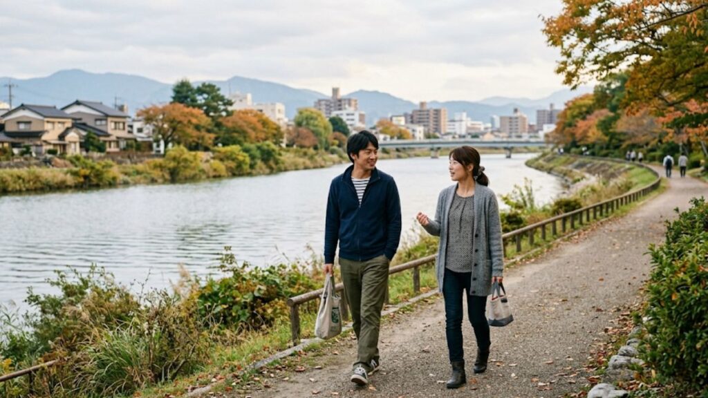 地方都市の穏やかな川沿いを歩きながら会話をする男女の様子。マッチングアプリの遠距離でつながった二人が、お互いを知っていく自然な風景です。