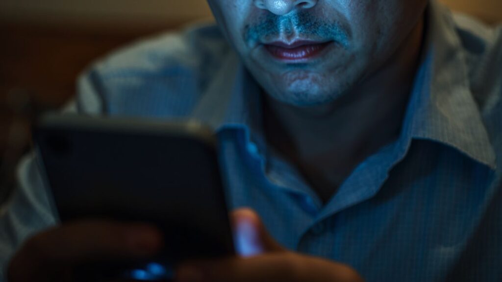 沖縄で出会いがない焦りから危険な掲示板トラブルに巻き込まれないよう、スマホを慎重に操作してリスクを回避しようとする男性。