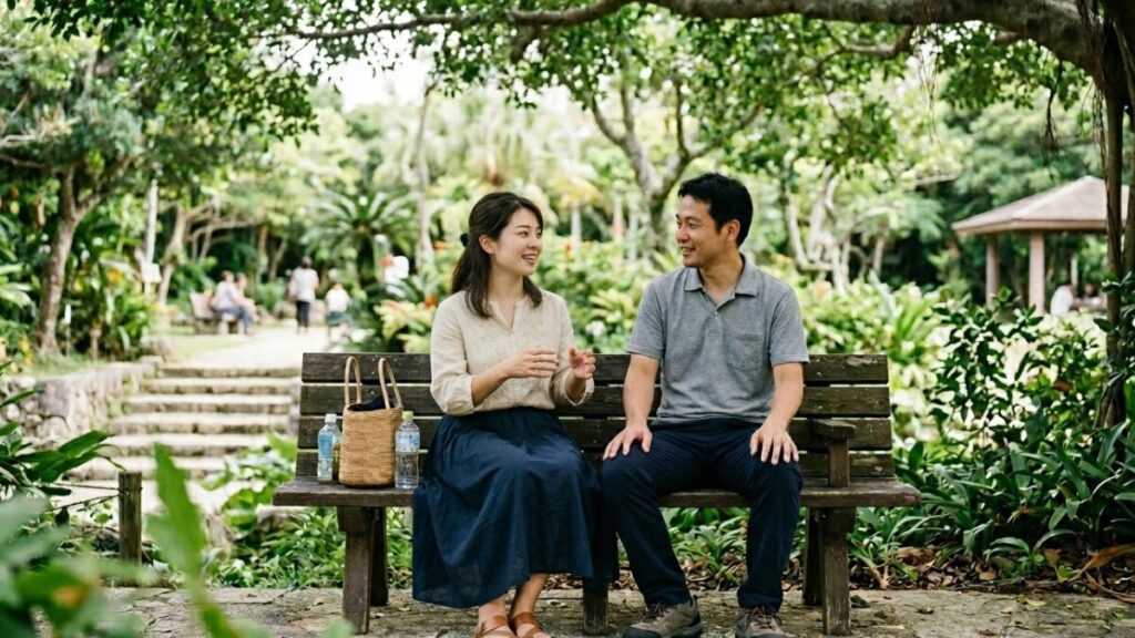 緑豊かな公園のベンチで、互いの時間を尊重し合いながら穏やかに話すカップル。沖縄女性の特徴をふまえ、協調性と人間的な温かさを重視する恋愛傾向を描写。