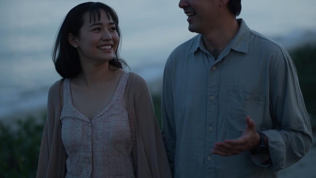 沖縄女性の特徴として好まれる、協調性があり人間味あふれる男性と、リラックスして海辺を歩くカップルの自然な情景。