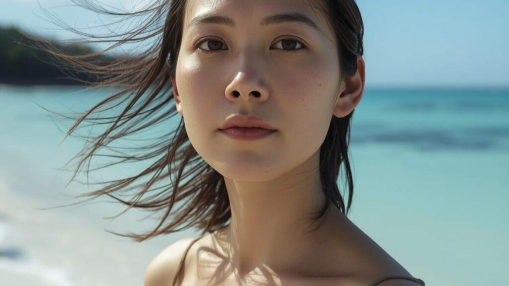 健康的な美しさを持つ沖縄女性の特徴をイメージした画像。美しい沖縄の海辺で心地よい海風を受ける、芯の強さを感じさせる女性の姿。